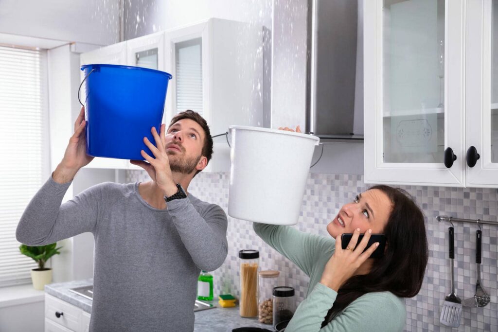 A man and woman holding buckets to catch water leaking from the kitchen ceiling.